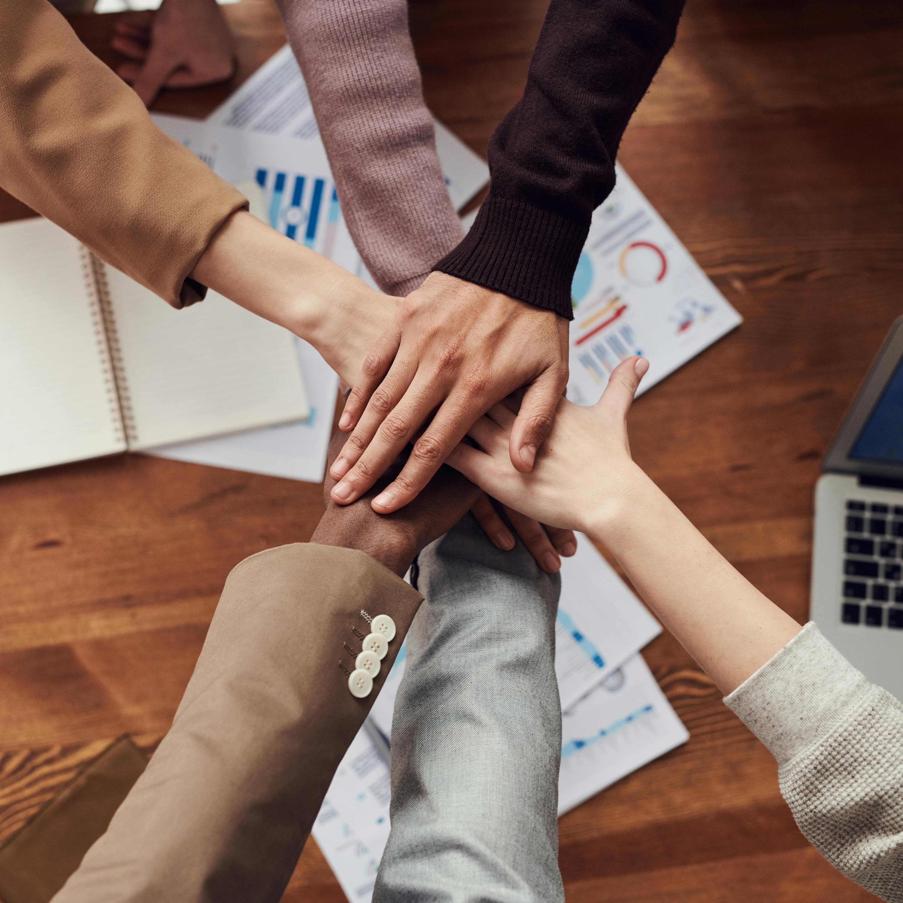 Várias pessoas esticando o braço e colocando as mãos uma sobre a outra, em sinal de união