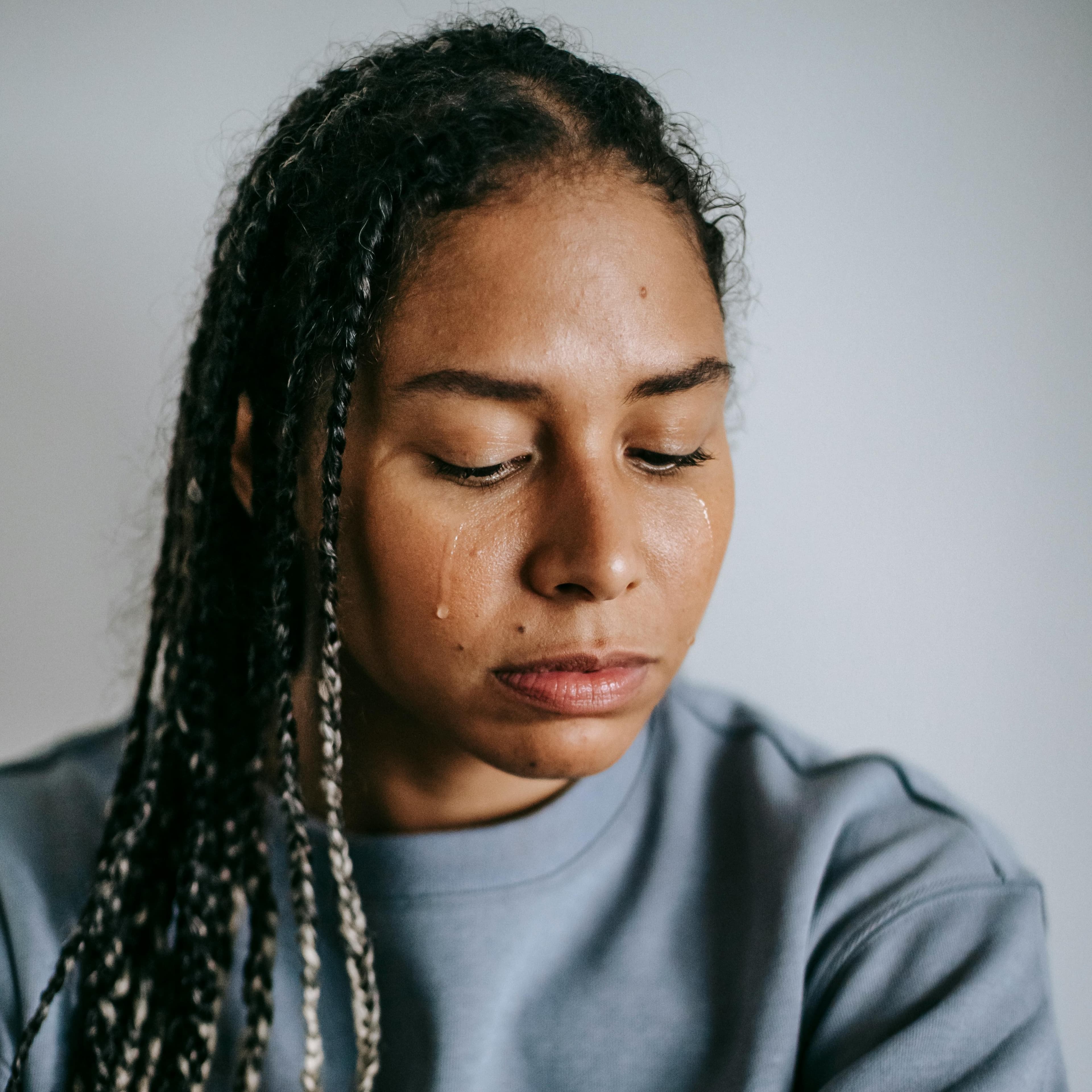 Mulher sentada no chão e abraçando as pernas está chorando