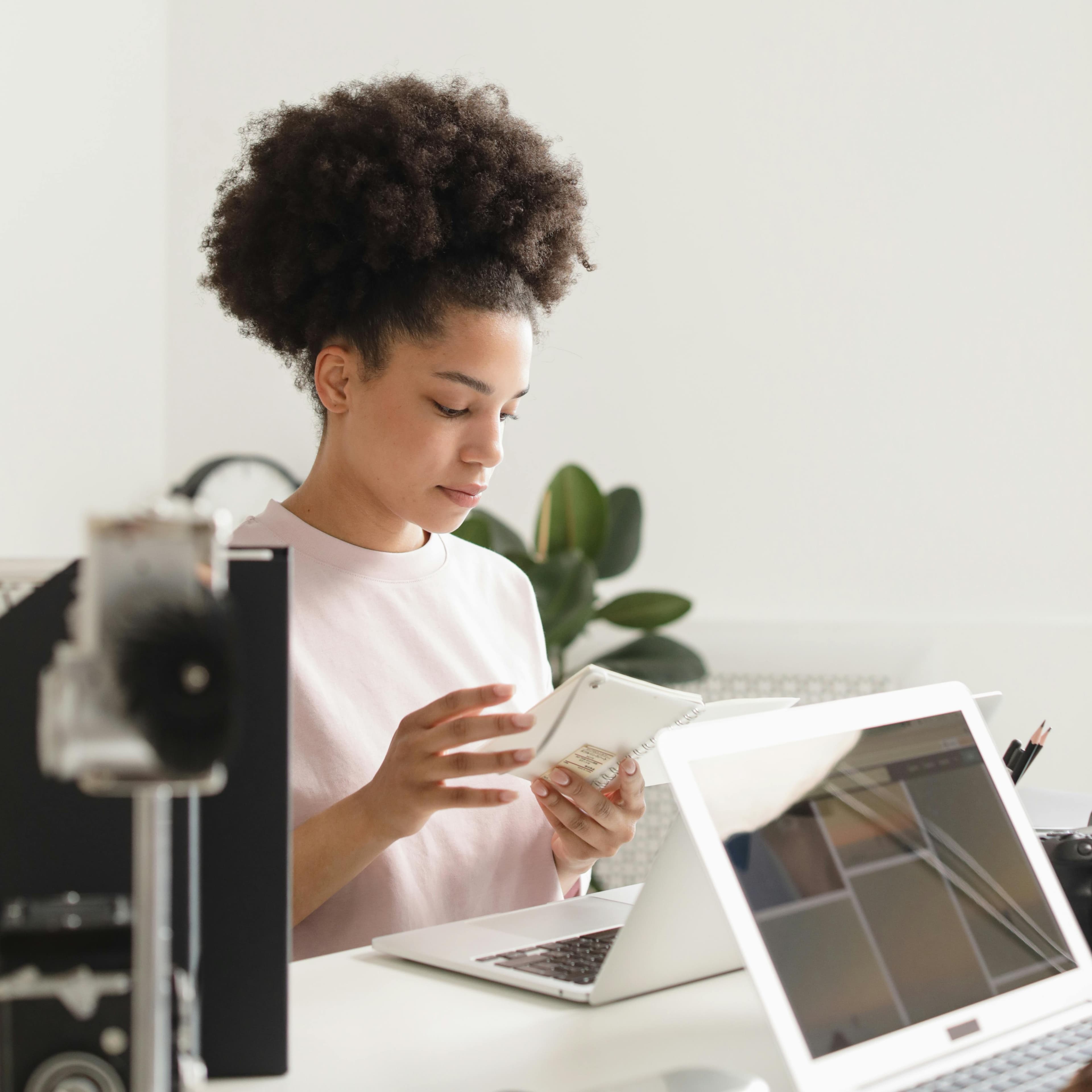 Mulher com sorriso mexendo no computador e fazendo anotações em sua caderneta